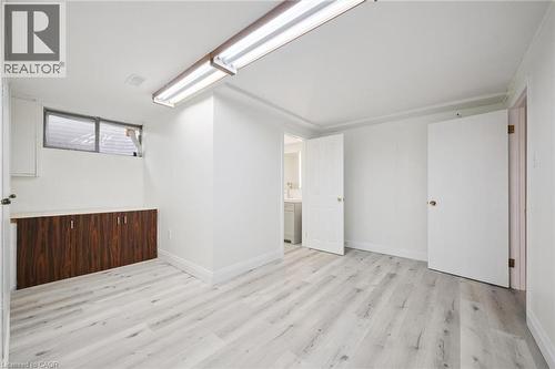 Brightly lit room featuring light wood-finish flooring, white walls, and a built-in cabinetry unit with dark wood-look doors - 27 Silverspring Crescent, Kitchener, ON - Indoor Photo Showing Other Room