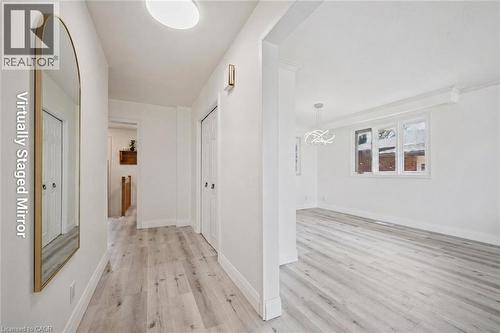 Light wood-finish flooring throughout, bright white walls, contemporary flush-mount ceiling light, modern wall sconce, and a geometric chandelier - 27 Silverspring Crescent, Kitchener, ON - Indoor Photo Showing Other Room