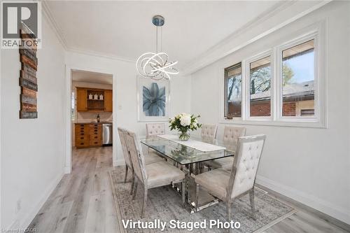 Bright dining area featuring wood-finish flooring, a contemporary chandelier, crown molding, and multiple windows - 27 Silverspring Crescent, Kitchener, ON - Indoor Photo Showing Dining Room
