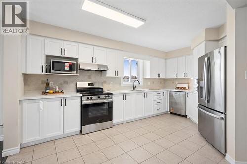 Kitchen featuring stainless steel appliances, white cabinets, light tile patterned floors, tasteful backsplash, and light stone counters - 649 Doon South Drive, Kitchener, ON - Indoor Photo Showing Kitchen