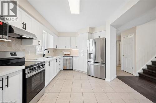Kitchen featuring stainless steel appliances, light tile patterned floors, white cabinetry, and decorative backsplash - 649 Doon South Drive, Kitchener, ON - Indoor Photo Showing Kitchen