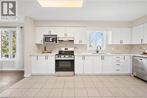 Kitchen featuring stainless steel appliances, white cabinets, light tile patterned flooring, and decorative backsplash - 649 Doon South Drive, Kitchener, ON - Indoor Photo Showing Kitchen