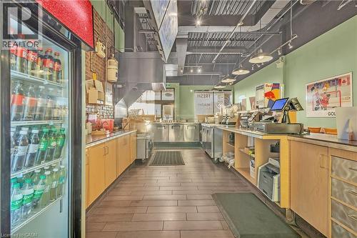 Commercial kitchen area featuring wood-finish flooring, light green walls, exposed brick accents, and a suspended ceiling with track lighting - 589 Fairway Road S, Kitchener, ON 