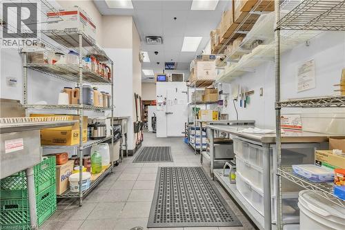 Commercial kitchen space featuring tile flooring, stainless steel fixtures, extensive wire shelving, and overhead fluorescent lighting - 589 Fairway Road S, Kitchener, ON 