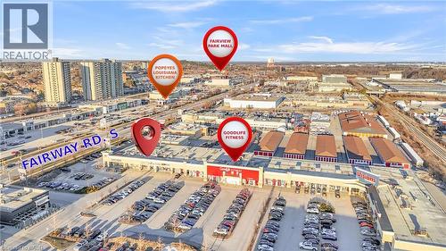 Aerial view highlighting the commercial district with multiple retail establishments, extensive parking areas, and adjacent multi-story residential buildings - 589 Fairway Road S, Kitchener, ON 