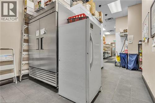 Commercial kitchen area featuring a large, stainless steel double-door refrigerator, a white upright refrigerator, and grey tile flooring - 589 Fairway Road S, Kitchener, ON 