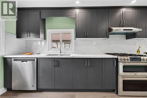 Contemporary kitchen featuring dark shaker-style cabinetry, light countertops, a stainless steel gas range with a matching range hood, a stainless steel dishwasher, and a double basin sink - 36 Mahony Avenue, Hamilton, ON - Indoor Photo Showing Kitchen With Double Sink With Upgraded Kitchen