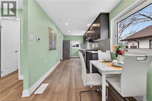 Contemporary kitchen and dining area featuring wood-finish flooring, recessed lighting, dark cabinetry, light countertops, and a stone-finish backsplash - 36 Mahony Avenue, Hamilton, ON - Indoor Photo Showing Dining Room