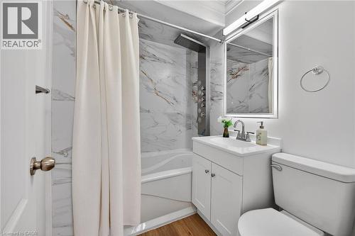 Bathroom featuring a white vanity with integrated sink, white marble-look wall tiling, a shower panel system, wood-finish flooring, and a mirrored medicine cabinet with integrated lighting - 36 Mahony Avenue, Hamilton, ON - Indoor Photo Showing Bathroom