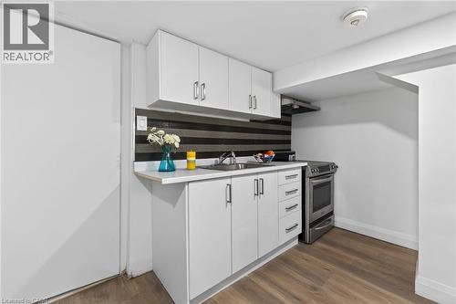 Compact kitchen featuring white cabinetry with silver-tone hardware, a white countertop, a stainless steel range, and wood-finish flooring - 36 Mahony Avenue, Hamilton, ON - Indoor Photo Showing Kitchen
