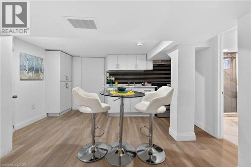Compact kitchen area featuring white cabinetry, a black and white striped tile backsplash, stainless steel appliances, and wood-finish flooring - 36 Mahony Avenue, Hamilton, ON - Indoor Photo Showing Dining Room