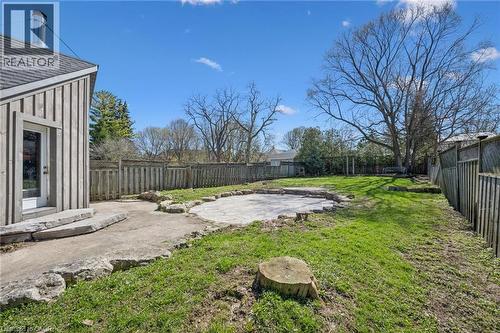 Expansive fenced backyard featuring a stone patio, mature trees, and a board-and-batten exterior wall with a glass-paneled door - 115 Allen Street E, Waterloo, ON - Outdoor With Backyard