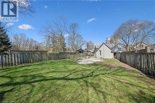 Expansive fenced backyard featuring a grassy lawn, a small concrete pad, and a separate structure with siding and a gable roof - 115 Allen Street E, Waterloo, ON - Outdoor With Backyard