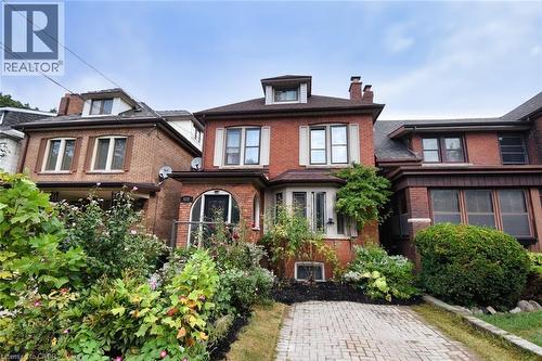 Brick exterior featuring a gabled roofline, bay windows, mature front garden, and a paver driveway - 522 Aberdeen Avenue, Hamilton, ON - Outdoor With Facade