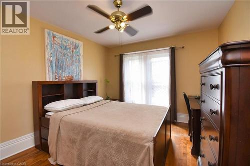 Bedroom featuring warm-toned walls, wood-finish flooring, a ceiling fan with integrated lighting, and a large window with sheer and blackout drapery - 522 Aberdeen Avenue, Hamilton, ON - Indoor Photo Showing Bedroom
