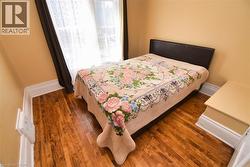Room featuring wood-finish flooring, light-colored walls, white baseboards, and a window with dark drapes - 