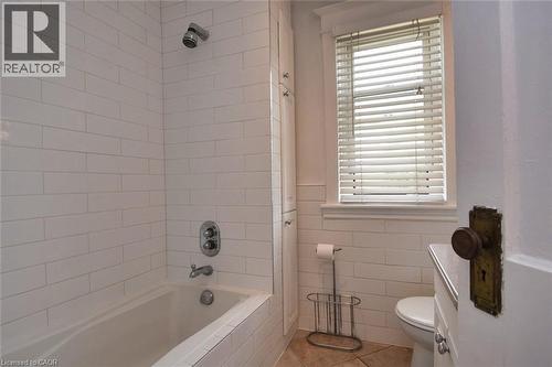 Bathroom featuring a tiled shower/tub combination with chrome fixtures, a window with horizontal blinds, built-in storage cabinetry, and a white commode - 522 Aberdeen Avenue, Hamilton, ON - Indoor Photo Showing Bathroom