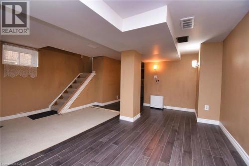Lower-level room featuring wood-finish flooring, a carpeted stairwell, and a window with brick exterior visible - 522 Aberdeen Avenue, Hamilton, ON - Indoor