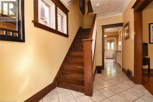 Wood staircase with a contrasting white baluster, tile flooring, and a framed mirror reflecting a chandelier - 522 Aberdeen Avenue, Hamilton, ON - Indoor Photo Showing Other Room