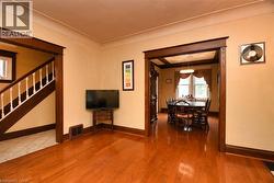 Spacious interior featuring warm wood-finish flooring, substantial dark wood trim, a wide doorway opening, a staircase with white balusters, and a visible dining area with a tray ceiling - 