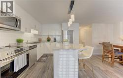 Contemporary kitchen featuring white cabinetry, stainless steel appliances, light granite countertops, a subway tile backsplash, and wood-finish flooring - 