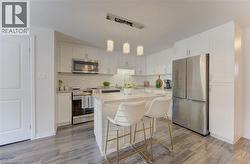 Modern kitchen featuring white cabinetry, stainless steel appliances, light-toned wood-finish flooring, a kitchen island with seating, and pendant lighting - 