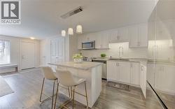 Open-concept kitchen featuring white cabinetry, granite countertops, stainless steel appliances, a subway tile backsplash, and wood-finish flooring - 