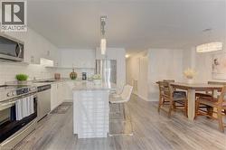 Open-concept kitchen featuring white cabinetry, stainless steel appliances, a subway tile backsplash, and a central island with a stone-finish countertop - 