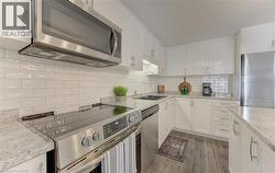 Contemporary kitchen featuring white cabinetry, stainless steel appliances, a white subway tile backsplash, light-toned countertops, and wood-finish flooring - 