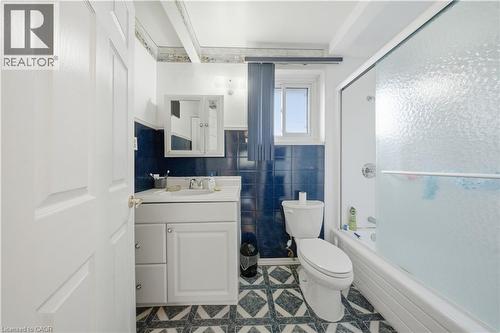 Bathroom featuring a white vanity with integrated sink, chrome faucet, white paneled door, blue tiled walls, and patterned floor tiling - 116 Gainsborough Road, Hamilton, ON - Indoor Photo Showing Bathroom