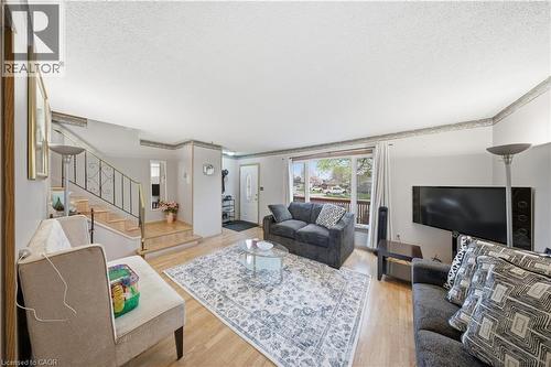 Bright living area featuring wood-finish flooring, a large picture window, and a staircase with an ornamental metal railing - 116 Gainsborough Road, Hamilton, ON - Indoor Photo Showing Living Room
