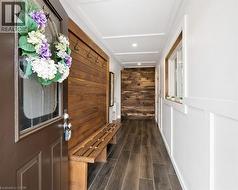 Welcoming entry hall featuring a solid panel door with decorative glass, wood-finish flooring, a built-in wooden bench with coat hooks, and an accent wall with varied wood paneling - 