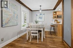 Dining area featuring wood-finish flooring, a tray ceiling with wood beams, and a modern geometric pendant light - 