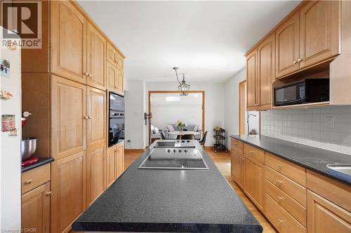 Kitchen featuring an expansive center island with an integrated cooktop, extensive wood cabinetry, dark countertops, and a white subway tile backsplash - 277 Blackacres Boulevard, London, ON - Indoor Photo Showing Kitchen