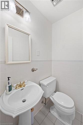 Bathroom featuring a pedestal sink with brass-finish fixtures, white tile flooring, white tiled walls, and a wall-mounted mirror - 277 Blackacres Boulevard, London, ON - Indoor Photo Showing Bathroom