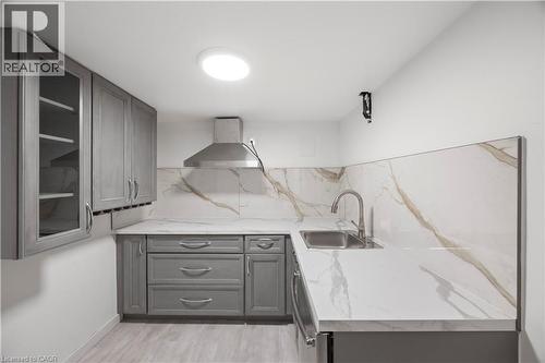 Kitchenette featuring light gray cabinetry, a stainless steel range hood, stone-finish countertops, a matching backsplash, and wood-finish flooring - 277 Blackacres Boulevard, London, ON - Indoor