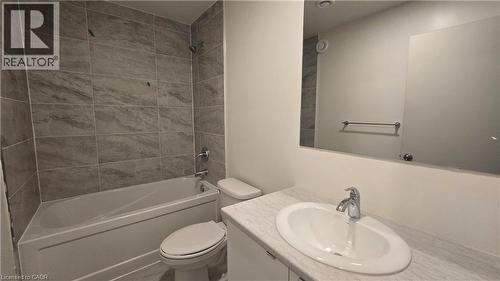 Bathroom featuring a white bathtub with tile surround, a built-in vanity with an undermount sink, a stone-finish countertop, and a large wall-mounted mirror - 16 Melbourne Avenue Unit# 210B, St. Catharines, ON - Indoor Photo Showing Bathroom