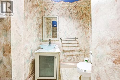 Powder room featuring a white vanity with a glass-front cabinet, a clear vessel sink with a chrome faucet, a wall-mounted mirror, and tile flooring - 116 Catharine Street S, Hamilton, ON - Indoor Photo Showing Bathroom