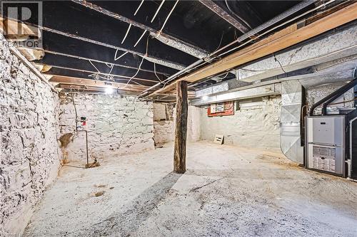 Unfinished basement space featuring stone foundation walls, exposed ceiling joists, a wood support column, and a visible furnace unit - 116 Catharine Street S, Hamilton, ON - Indoor Photo Showing Basement