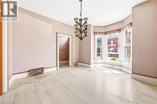 Room featuring a prominent bay window with natural light, light wood-finish flooring, and a decorative multi-arm chandelier - 116 Catharine Street S, Hamilton, ON - Indoor Photo Showing Other Room