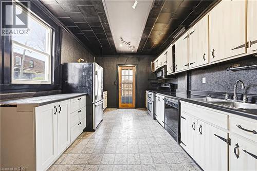 Galley kitchen featuring white cabinetry, black countertops, and a full suite of appliances including a refrigerator, dishwasher, and range - 116 Catharine Street S, Hamilton, ON - Indoor Photo Showing Kitchen With Double Sink