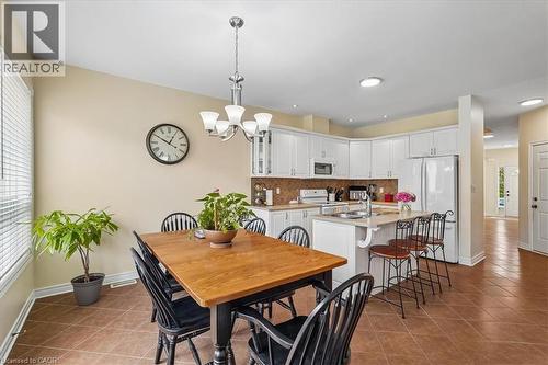 Open-concept kitchen and dining area featuring white cabinetry, a central island with integrated seating, stainless steel appliances, and a tiled backsplash - 4679 Webb Street, Burlington, ON - Indoor Photo Showing Dining Room