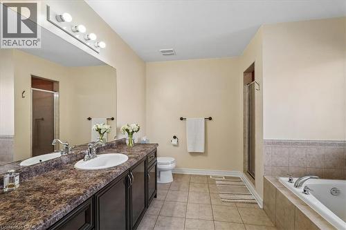 Spacious bathroom featuring a double vanity with dark wood cabinetry and a large mirror, a separate glass-enclosed shower, a soaking tub with tiled surround, and neutral floor tiling - 4679 Webb Street, Burlington, ON - Indoor Photo Showing Bathroom