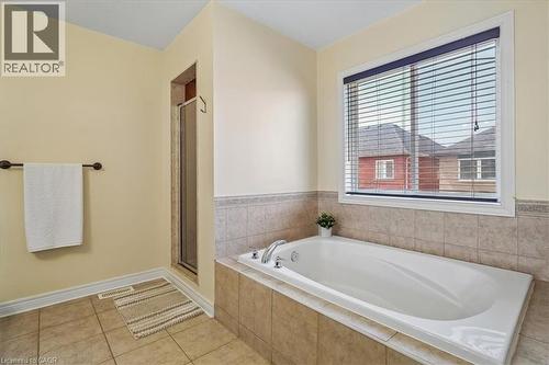 Bathroom featuring a built-in bathtub with integrated fixtures, ceramic tile surround, and a large window with blinds - 4679 Webb Street, Burlington, ON - Indoor Photo Showing Bathroom