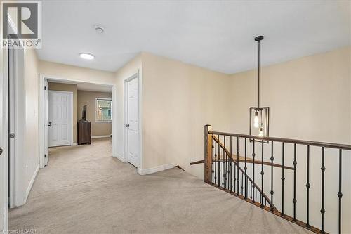 Upper-level landing featuring neutral carpeting, a staircase with dark wood railing and wrought iron spindles, and a modern pendant light fixture - 4679 Webb Street, Burlington, ON - Indoor Photo Showing Other Room