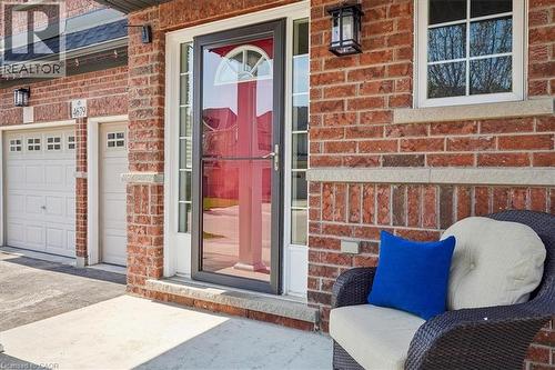 Brick exterior featuring a storm door with an arched transom, a window with grid detailing, and two garage doors with square window inserts - 4679 Webb Street, Burlington, ON - Outdoor With Exterior