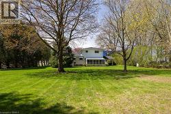 Expansive green lawn framed by mature trees, featuring a white two-story residence with a screened porch and a covered patio - 