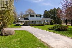 Two-story residence featuring a carport, front yard with manicured lawn and mature shrubs, and an asphalt driveway - 
