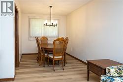 Dining area featuring wood-finish flooring, a modern chandelier with multiple light sources, and a large window with privacy blinds - 
