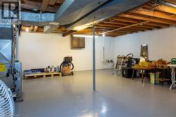 Spacious unfinished basement featuring exposed ceiling joists, concrete flooring, white panel walls, and visible ductwork - 